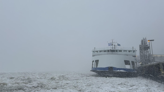Dans une tempête de neige, entouré d'amas de glaces flottantes, un navire est amarré au quai d'embarquement des passagers.