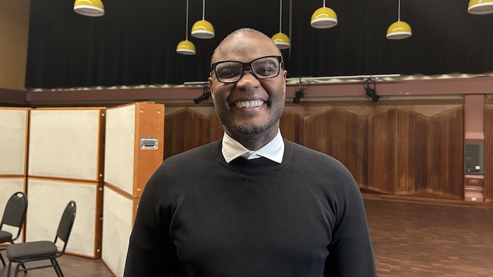 Trésor Otshudi se trouve dans un studio d'enregistrement. Il sourit à la caméra.