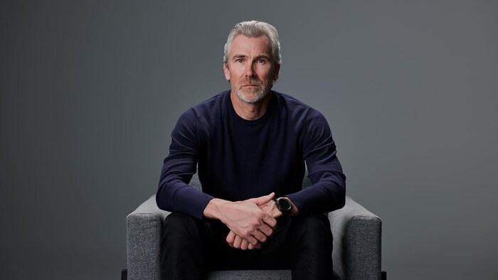 Trevor Linden assis sur un fauteuil dans un décor sombre.