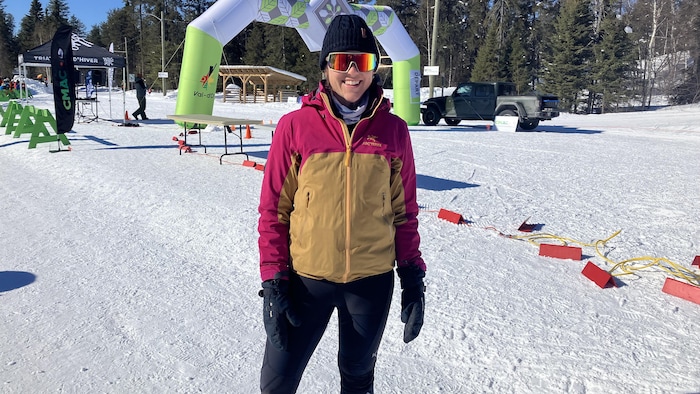 Anne-Marie Nadeau, lunettes de soleil sur les yeux et tuque sur la tête, pose pour la caméra sur la neige en affichant un grand sourire.