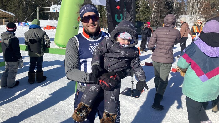 Xavier Perreault sourit à la caméra en tenant sa petite fille dans ses bras.
