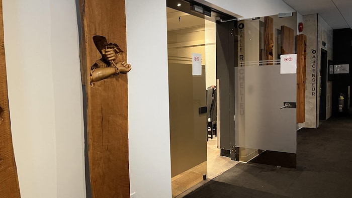 Une porte ouverte dans un couloir laisse entrevoir des chaises dans une salle.