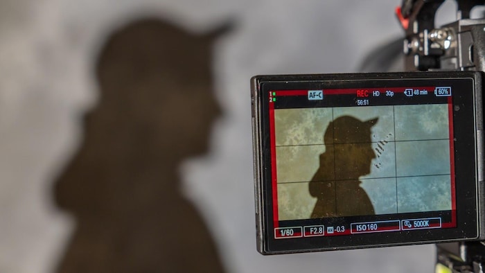 Une ombre projetée sur un mur et sur un écran de caméra.