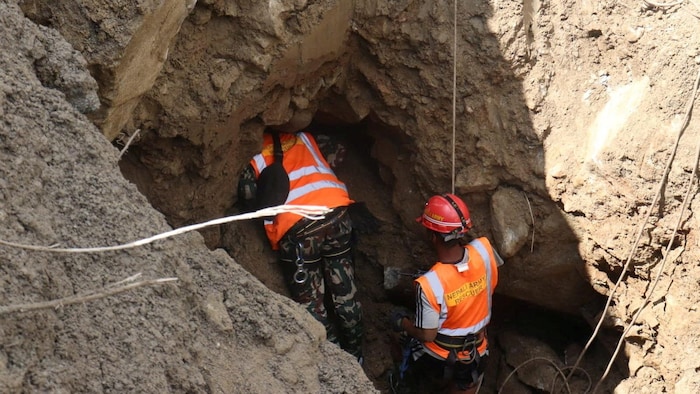 Deux secouristes portant des casques travaillent dans le fond d'un trou dans le sol.