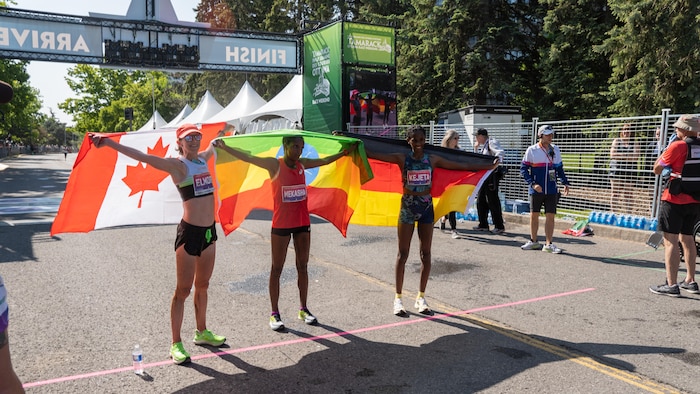 Les trois coureuses qui ont complété le marathon d'Ottawa soulèvent fièrement derrière elles le drapeau de leur pays d'origine, près de la ligne d'arrivée. 