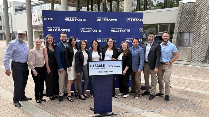12 personnes derrière un lutrin aux couleurs du parti. 