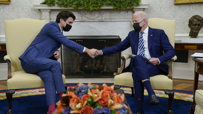 Justin Trudeau and Joe Biden, seated in the Oval Office, shake hands.