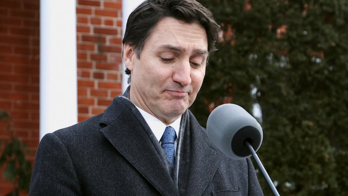 Justin Trudeau, tête baissée, devant un micro.