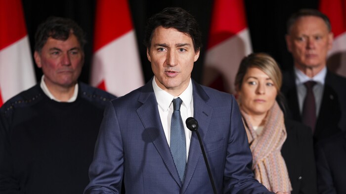 Justin Trudeau parle dans un micro avec notamment, derrière lui, Dominic LeBlanc et Mélanie Joly.