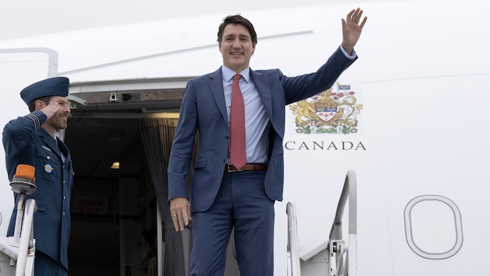Justin Trudeau salue de la main à côté de l'entrée d'un avion.