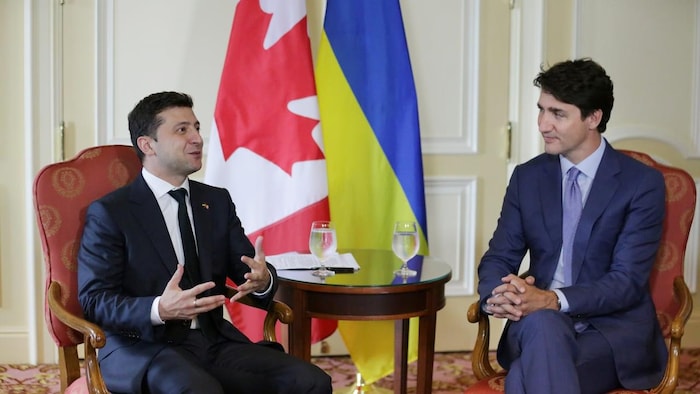 حديث بين رئيس الحكومة الكندية جوستان ترودو (إلى اليمين) والرئيس الأوكراني فولوديمير زيلينسكي، وكل منهما جالس على مقعد وبينهما علما كندا وأوكرانيا.