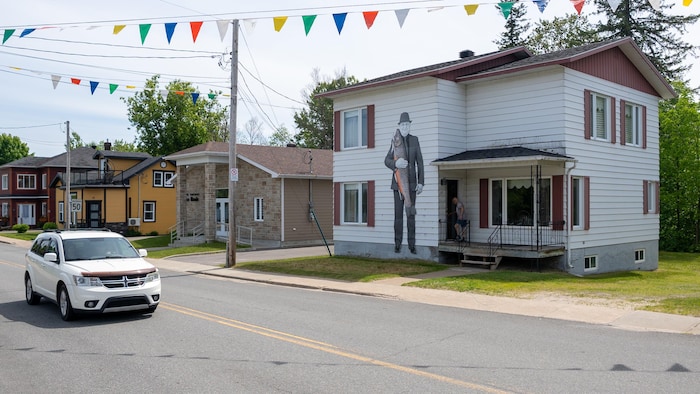Une immense photographie du chef des pompiers de Saint-Alexis-des-Monts, Raymond Beaudoin, tenant dans ses bras une truite géante est installée sur la façade d'une maison de deux étages.