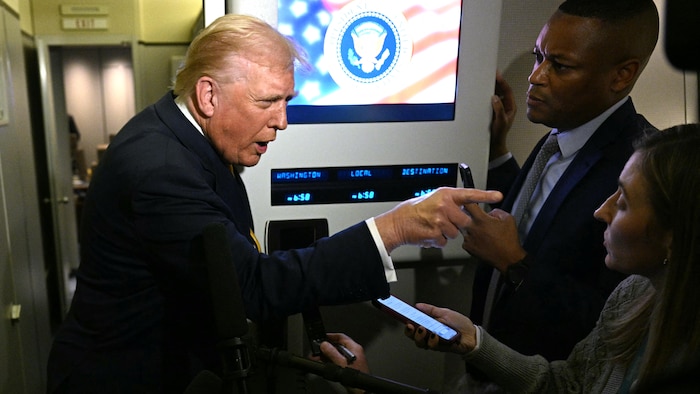 À bord d'Air Force One, Donald Trump montre quelqu'un du doigt devant des journalistes.