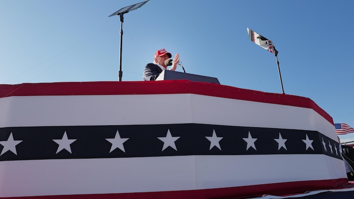 Donald Trump en train de s'adresser à la foule depuis une tribune décorée du drapeau américain. 
