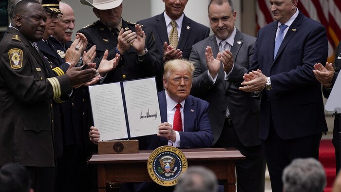 Donald Trump tient un décret dans ses mains et est applaudi par plusieurs personnes qui l'entourent.