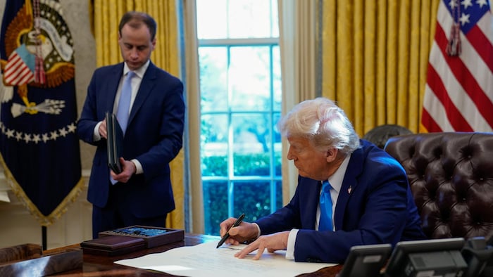 O presidente dos EUA, Donald Trump, assinou um documento no Salão Oval da Casa Branca em frente a um de seus colaboradores.
