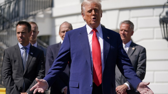 Donald Trump, devant un groupe d'hommes, prend la parole, les bras ouverts.