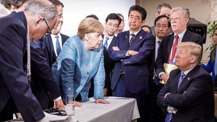 Donald Trump, assis les bras croisés, semble se faire gronder par Angela Merkel, debout devant lui.