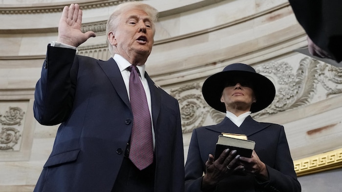 Donald Trump lève la main droite sans mettre la gauche sur la Bible, que tient Melania Trump, qui porte un vaste chapeau.