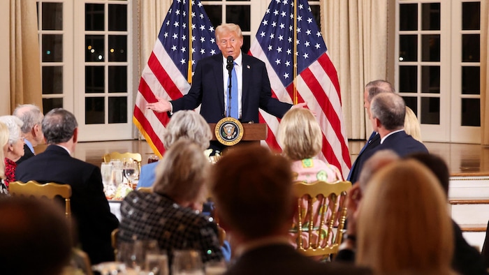 Donald Trump, devant des drapeau américains, s'adresse à des gens attablés devant lui.