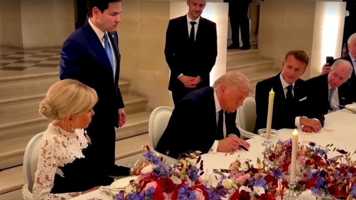 Donald Trump signe un document assis à une table à laquelle se trouve notamment le président français, Emmanuel Macron.
