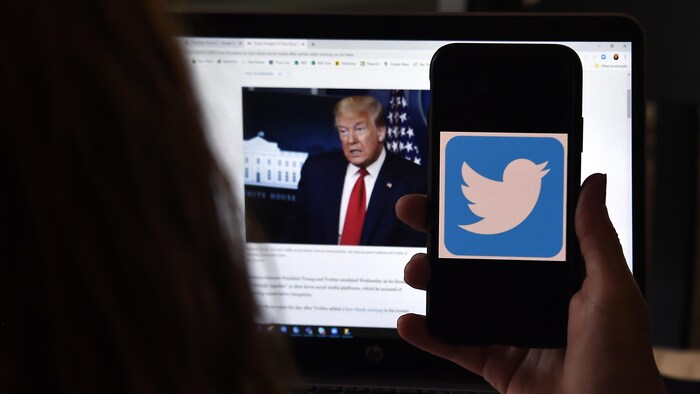 Le logo de Twitter apparaît sur l'écran d'un téléphone portable avec en image de fond une photo de Donald Trump.