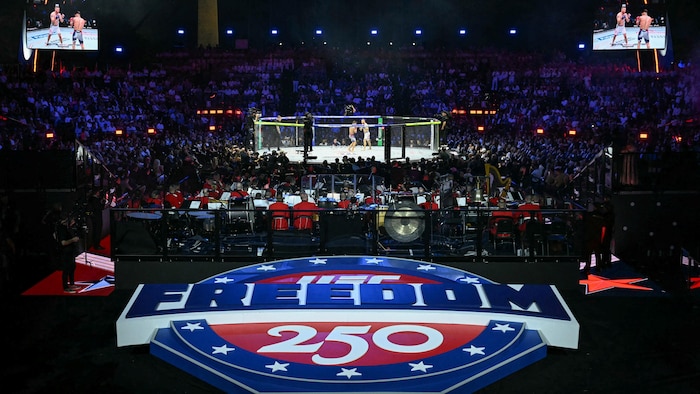 Deux hommes combattent dans un ring octogonal devant une foule, avec à l'avant-plan le mot « liberté ».