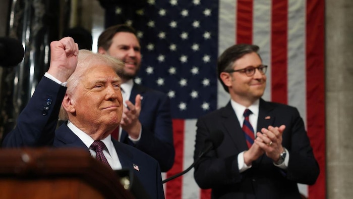 M. Trump pointe lève le poing et sourit sous les applaudissements de deux hommes.