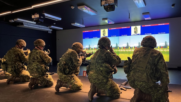 Des recrues en uniforme tirent virtuellement vers un écran lumineux qui simule des cibles.
