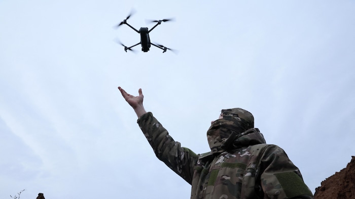 Un soldat que survole un drone, dans une tranchée.