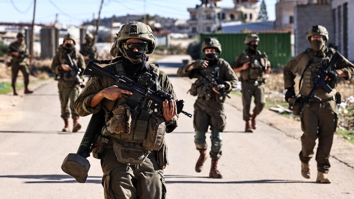 Une dizaine de soldats armés marchent dans la rue.