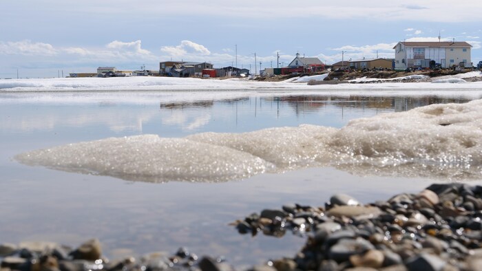Un village sur la côte derrière une étendue d’eau à moitié gelée.