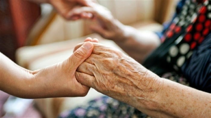 Gros plan sur les mains d'une préposée aux bénéficiaires qui tiennent celles d'une personne âgée.