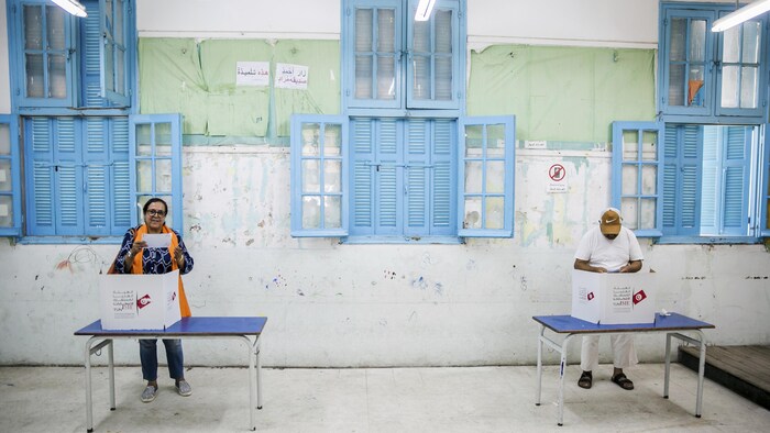 Un homme et une femme préparent leur bulletin de vote dans des isoloirs.