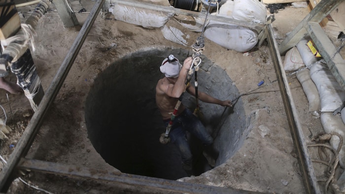 Un ouvrier, attaché par un harnais, s'apprête à être descendu dans un tunnel vertical.