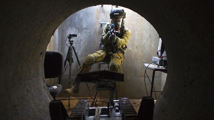 Dans un tunnel, un soldat pointe un fusil sur un robot.