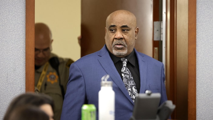 Duane Davis, en complet, entre dans une salle d'audience, suivi de près par un agent de la paix.