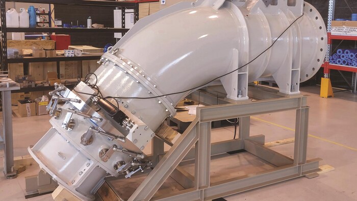 Un tuyau blanc légèrement courbé vers le bas est présenté sur un support dans une usine.