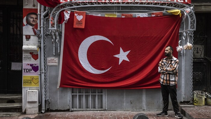 Un homme est debout devant un drapeau turc.