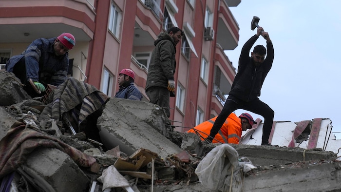 De jeunes hommes travaillent dans les ruines près de secouristes.