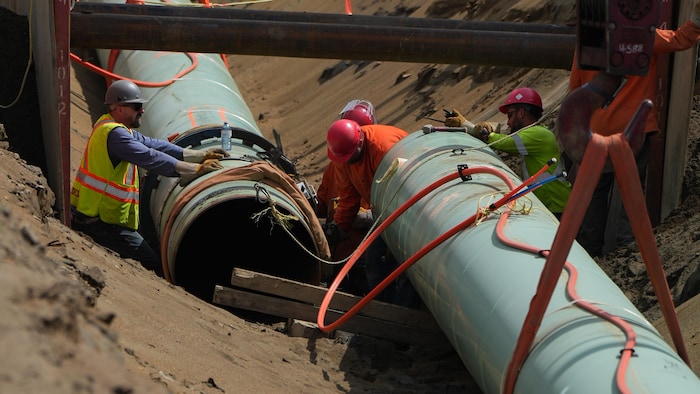 Des ouvriers en casques de sécurité raccordent un grand tuyau au fond d'une tranchée de chantier.