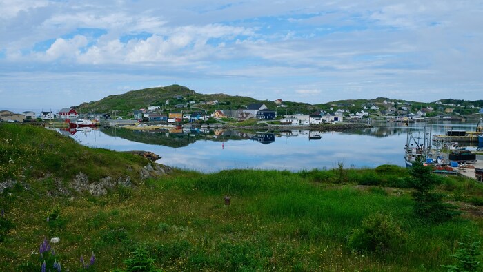 Photo d'une petite communauté au bord de l'eau. Les maisons et les nuages se reflètent dans l'eau.