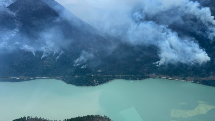 Lac émeraude avec de la fumée dans les montagnes au-dessus.