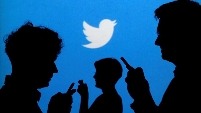 Des silhouettes de personnes tenant des téléphones intelligents devant une murale bleue arborant le logo de Twitter.