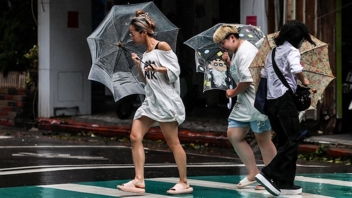 Des piétons, parapluie à la main, traversent une rue sous une pluie battante et des vents violents alors que le typhon Bavi passe au large du nord-est de Taïwan, à Keelung, le 11 juillet 2026.