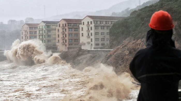 Des vagues de plusieurs mètres de haut frappent une digue devant des bâtiments. 