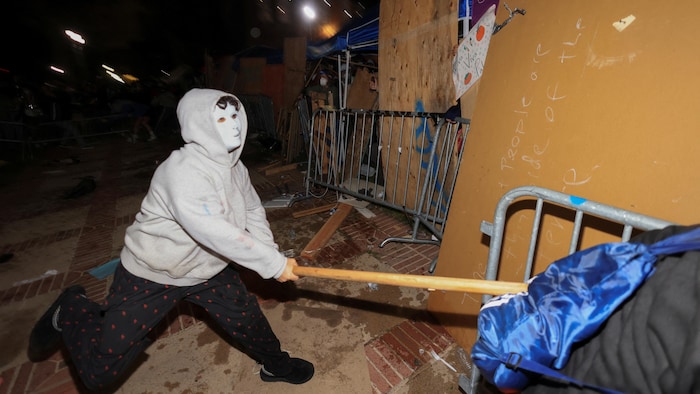 Un manifestant masqué frappe à coup de bâton sur une clôture de sécurité.