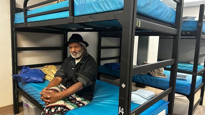 Un homme assis sur un lit dans un dortoir. 