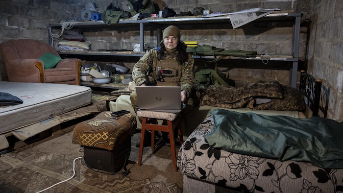 Une femme habillée en soldat utilise un ordinateur dans un abri.