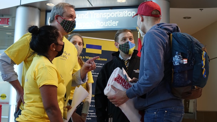 Un homme avec un sac à dos dans un aéroport en conversation avec le premier ministre de la province Andrew Furey et son équipe.